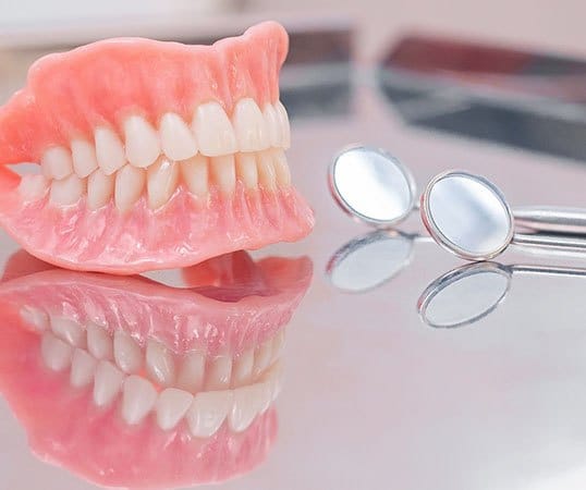 Denture on a reflective table next to dental mirror