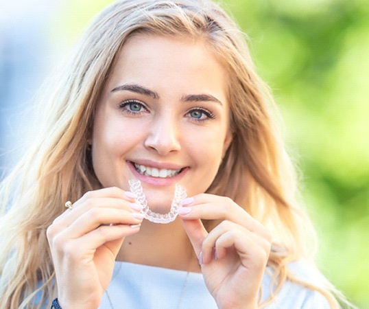 young woman smiling while holding Invisalign aligner