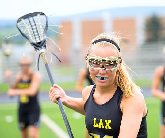 Teen girl playing lacrosse with blue athletic mouthguard in palce