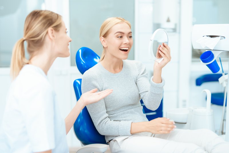 a female patient looking at her new smile in the mirror while listening to her cosmetic dentist