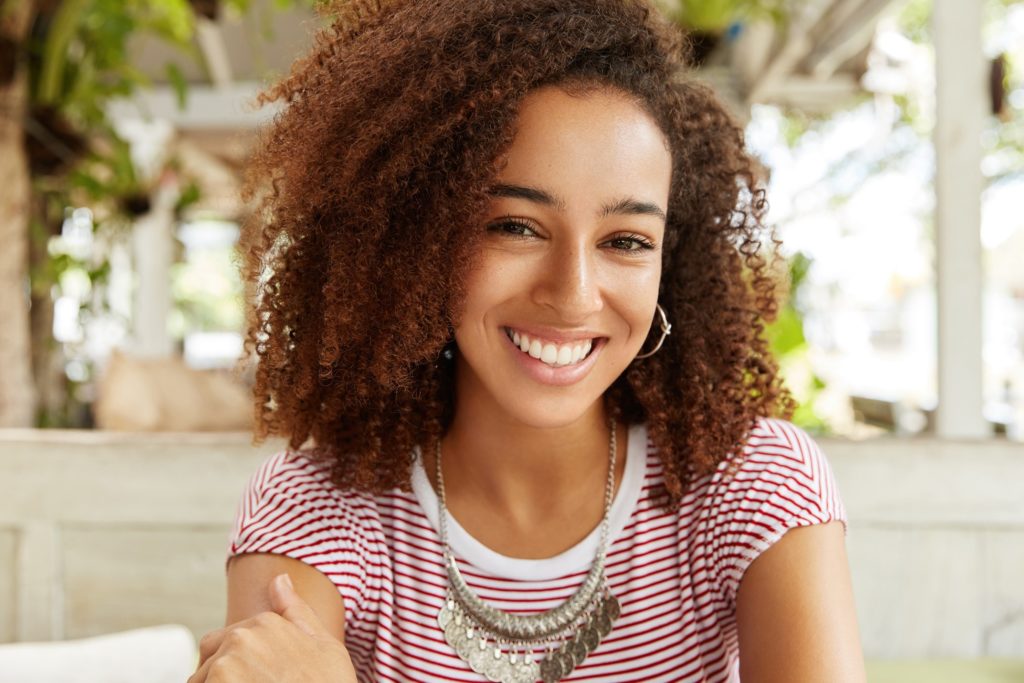 Woman with white, straight, beautiful teeth smiling outside