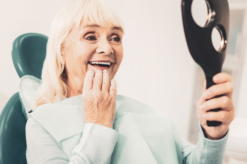 A closeup of a senior woman admiring her dentures in a hand mirror