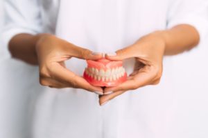 Woman in white blurry in the background holding a set of dentures with 2 hands in the foreground